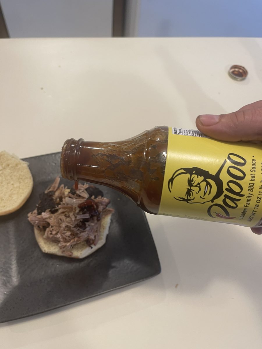 Pouring Papoo's Original over a pulled pork sandwich