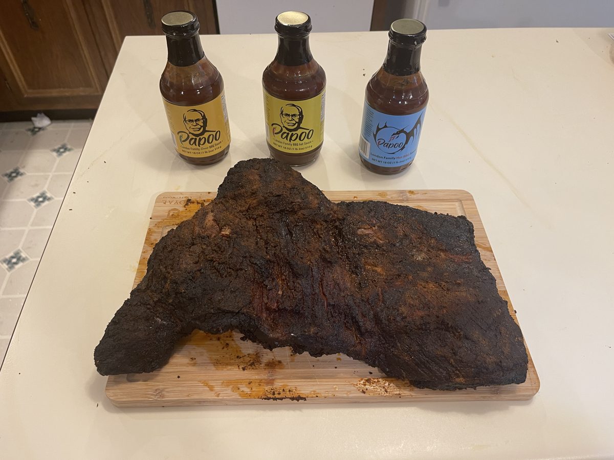 A whole smoked brisket on a cutting board with three bottles of Papoo's