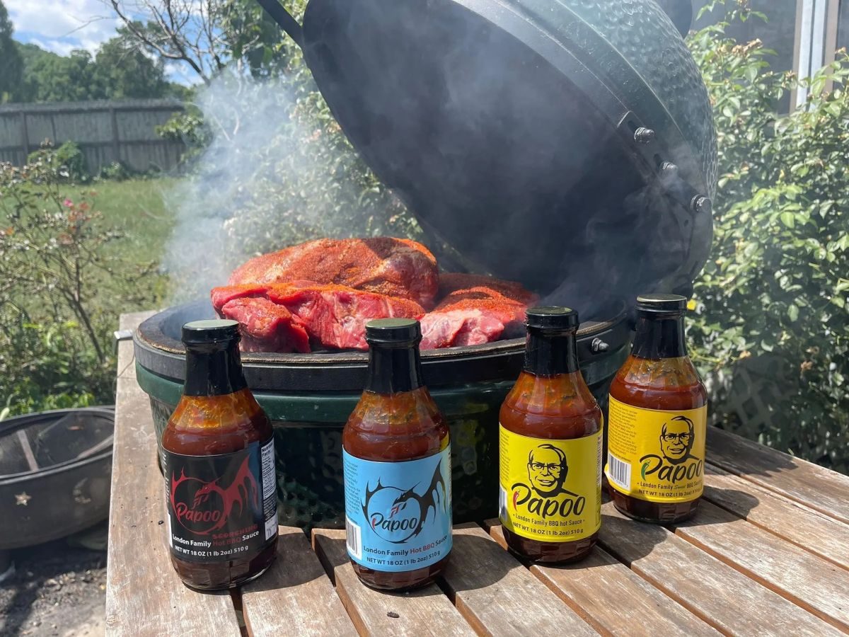 Pork on a smoking grill with all four Papoo's BBQ sauces lined up in front