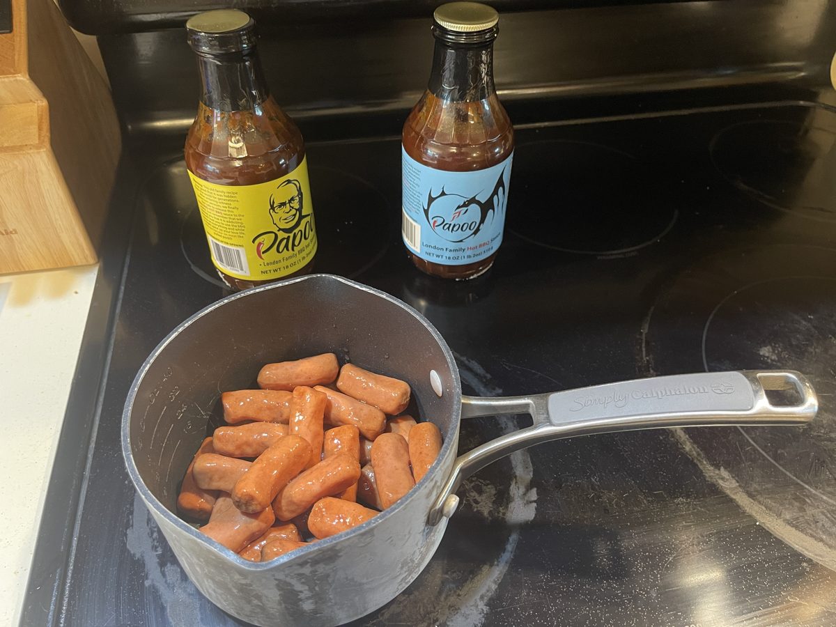 Mini wieners browning in a pot with bottles of Papoo's behind